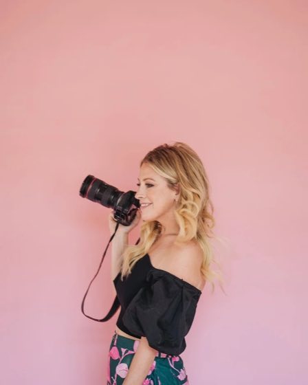 Hope Kauffman holding her camera against a pink studio backdrop.